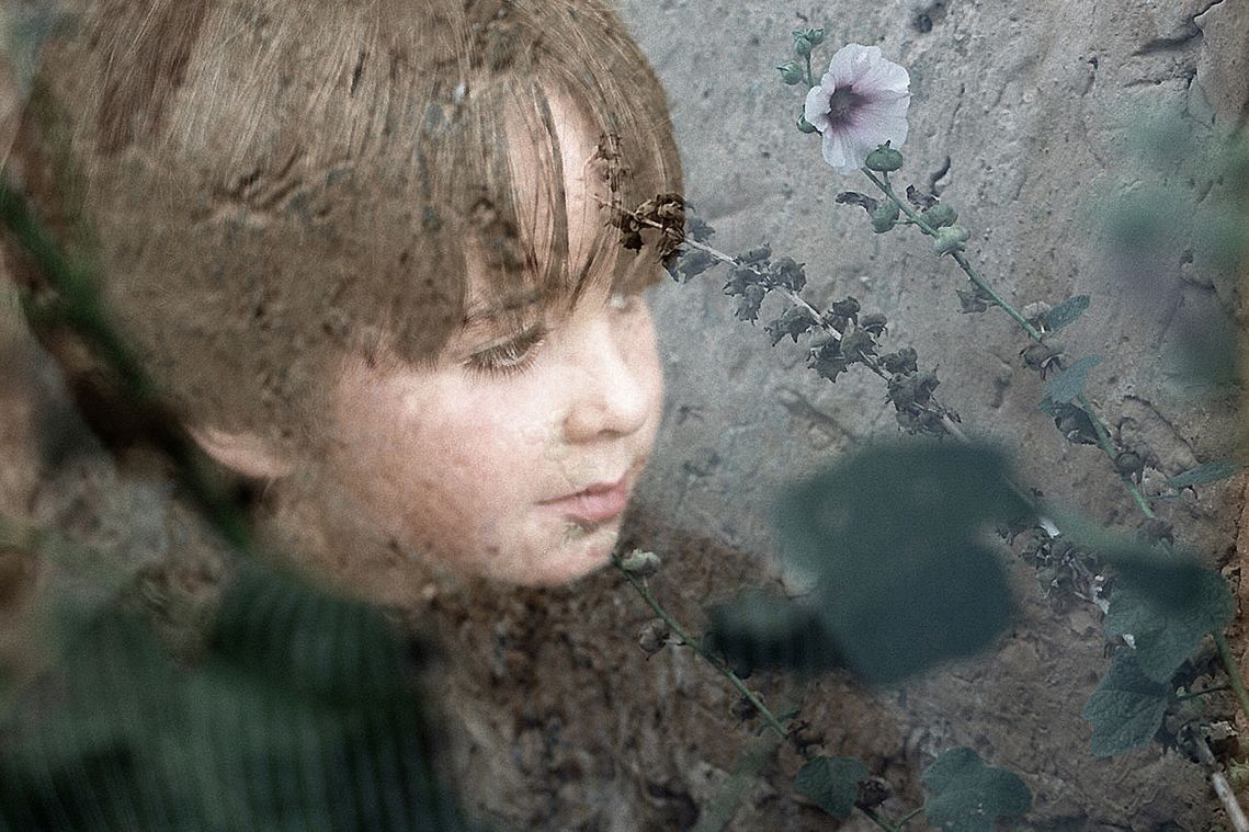 portrait couleur d'un enfant sur un mur en fond avec une fleur.