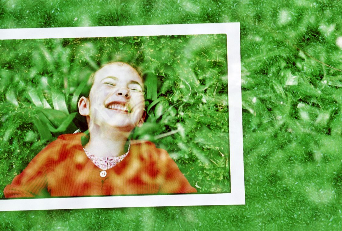 Photographie d'un visage de petite fille riant sur fond d'herbe.