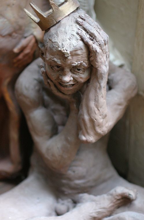 Photographie d'une sculpture d'un personnage assis en tailleur se tenant la tête ornée d'une couronne.