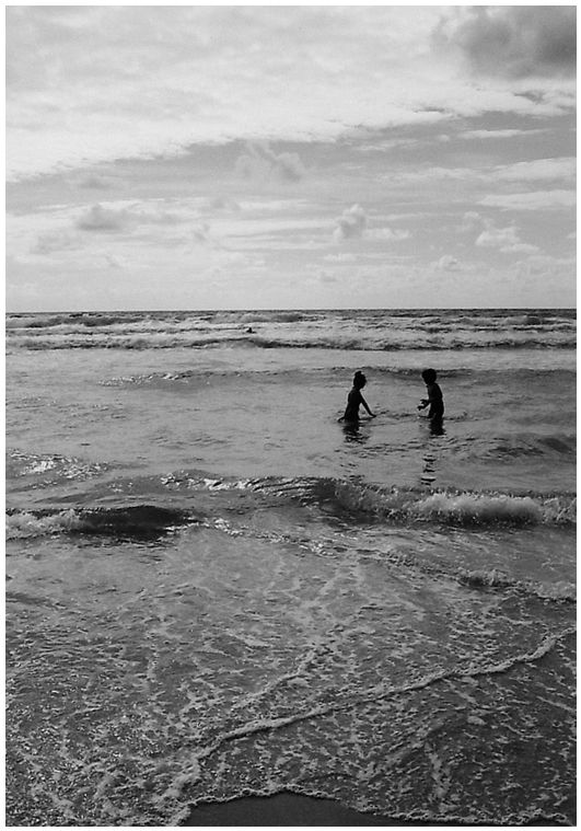 photographie noir et blanc de deux silhouettes d'enfants au loin dans la mer.