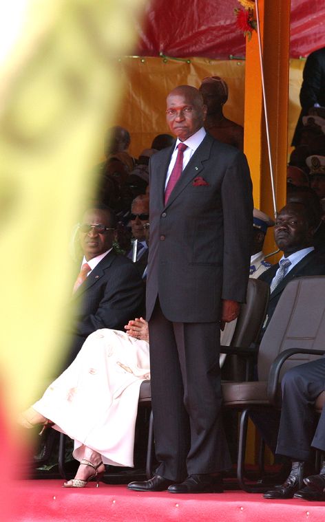 Photo d'abdoulaye wade debout avec amorce d'un drapeau au premier plan.