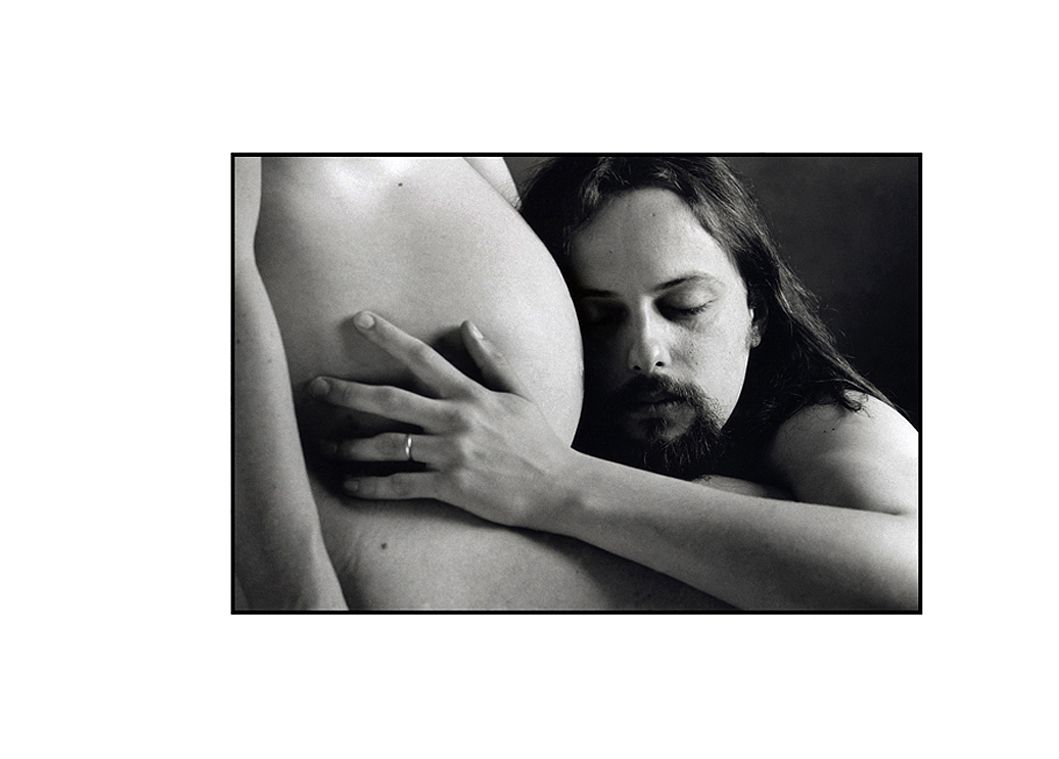 Photo noir et blanc d'un père écoutant le ventre de sa femme enceinte.