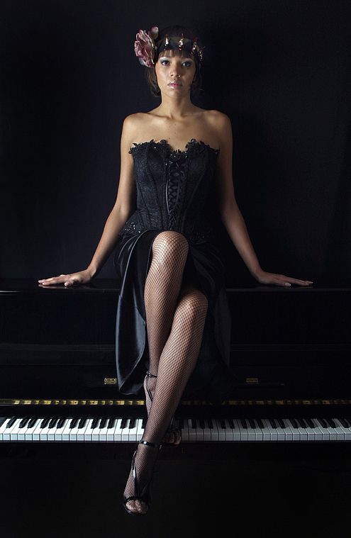 photo couleur d'une jeune femme en robe noire assise sur un piano.